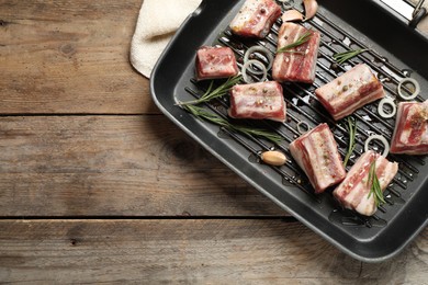 Photo of Grill pan with raw ribs and seasonings on wooden table, top view. Space for text