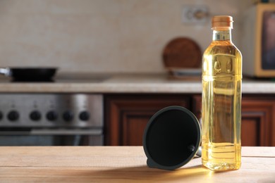 Photo of Bottle of cooking oil and funnel on wooden table in kitchen, space for text