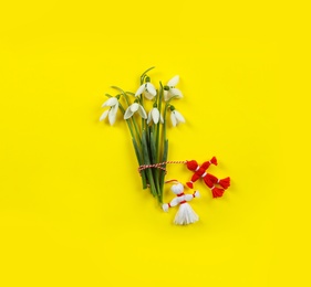 Beautiful snowdrops with traditional martisor on yellow background, flat lay. Symbol of first spring day