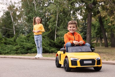 Cute girl operating children's car with little boy outdoors