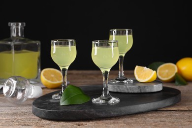 Photo of Tasty limoncello liqueur, lemons and green leaves on wooden table