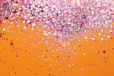 Photo of Shiny bright pink glitter on orange background, flat lay