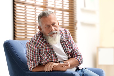 Photo of Portrait of handsome mature man sitting in armchair indoors