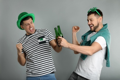 Emotional men in St Patrick's Day outfits with beer on light grey background
