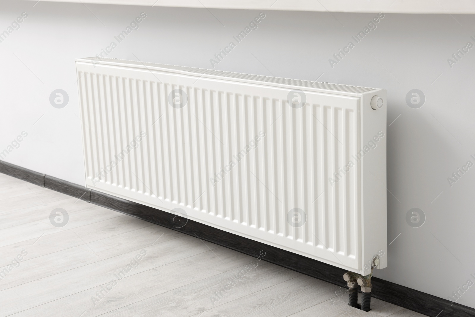 Photo of Modern radiator on white wall in room. Central heating system