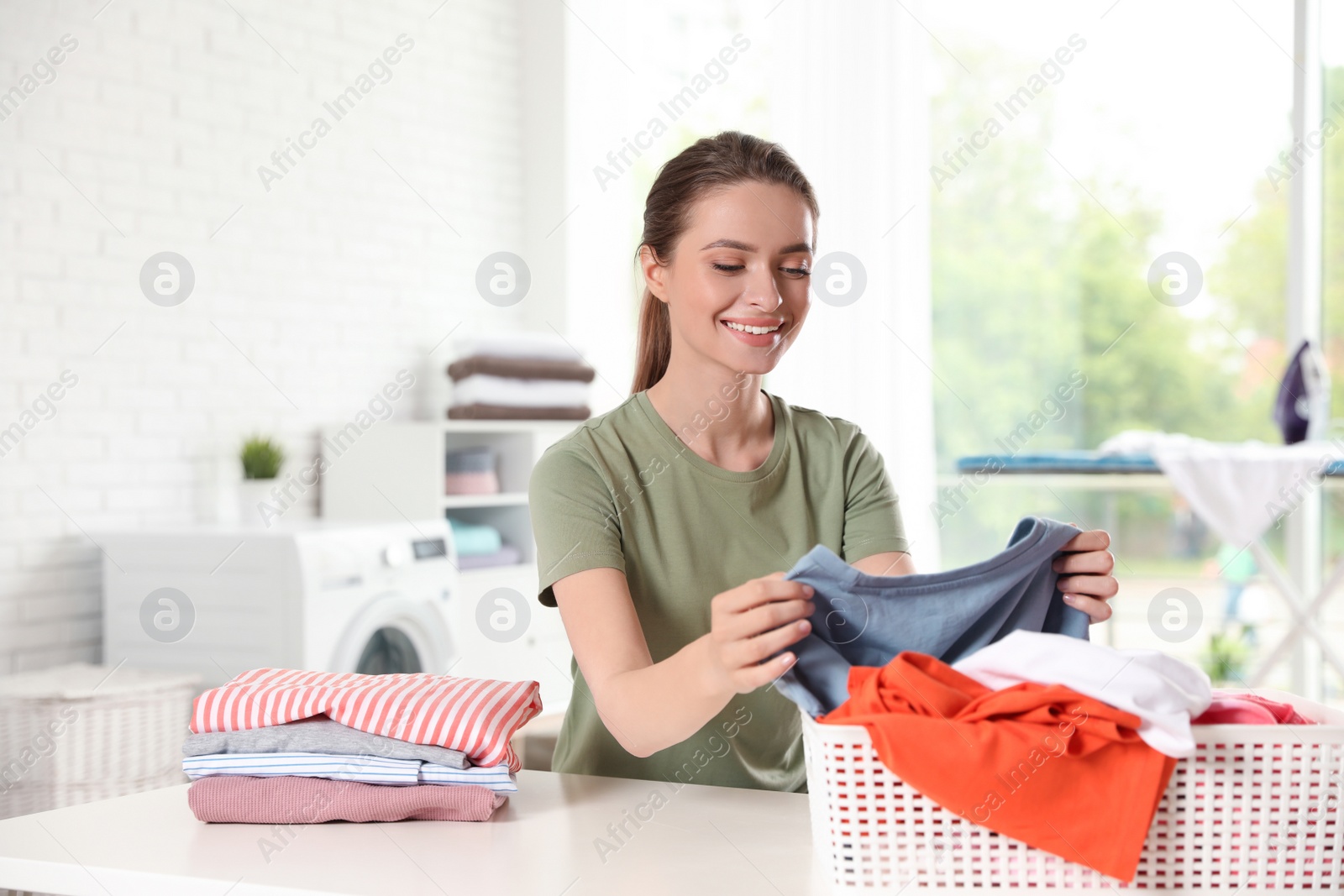 Photo of Happy woman with clean laundry at table indoors