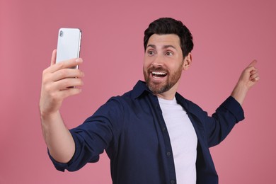 Photo of Smiling man taking selfie with smartphone on pink background