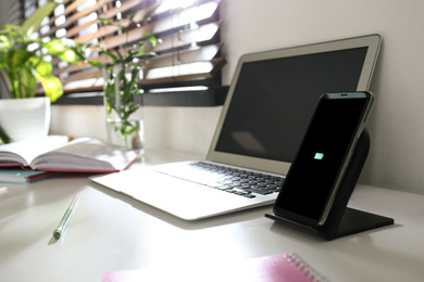 Photo of Modern workplace and smartphone charging with wireless pad