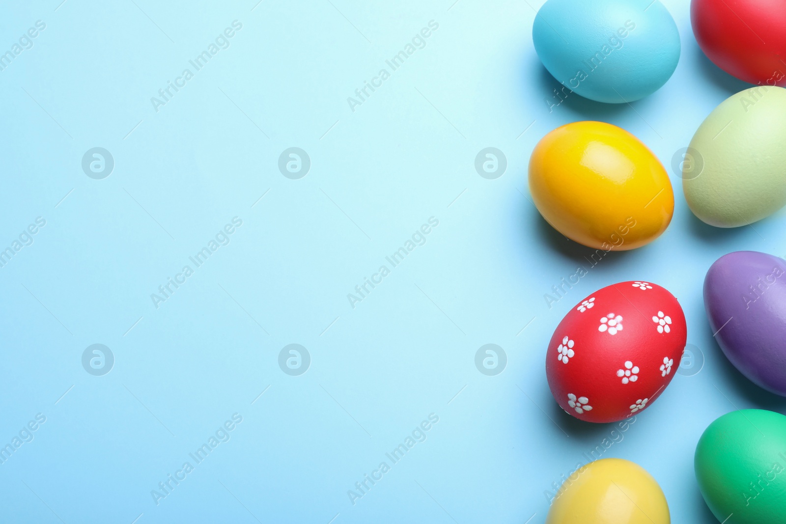 Photo of Bright painted eggs on light blue background, flat lay with space for text. Happy Easter