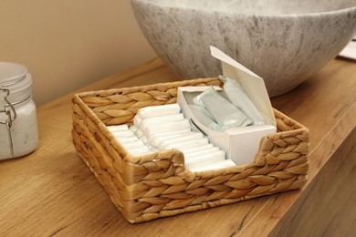 Photo of Wicker basket with many different tampons on wooden countertop in bathroom, closeup. Menstrual hygienic product
