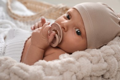 Photo of Adorable newborn baby with pacifier in wicker basket, closeup