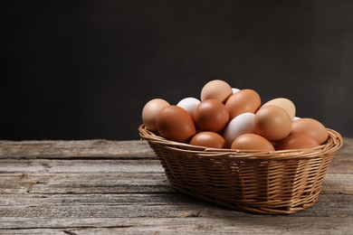 Fresh chicken eggs in wicker basket on wooden table. Space for text