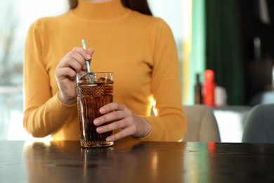 Woman with glass of refreshing cola at table indoors, closeup. Space for text