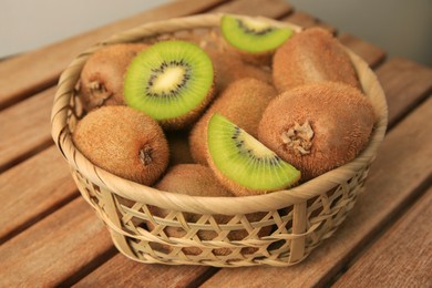 Wicker basket with whole and cut kiwis on wooden table, closeup