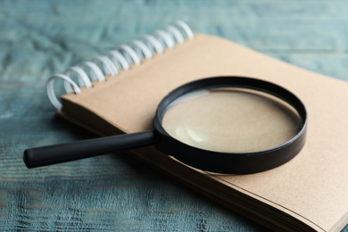 Photo of Magnifier glass and empty notebook on light blue wooden background, closeup. Find keywords concept