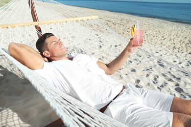 Man with refreshing cocktail relaxing in hammock on beach