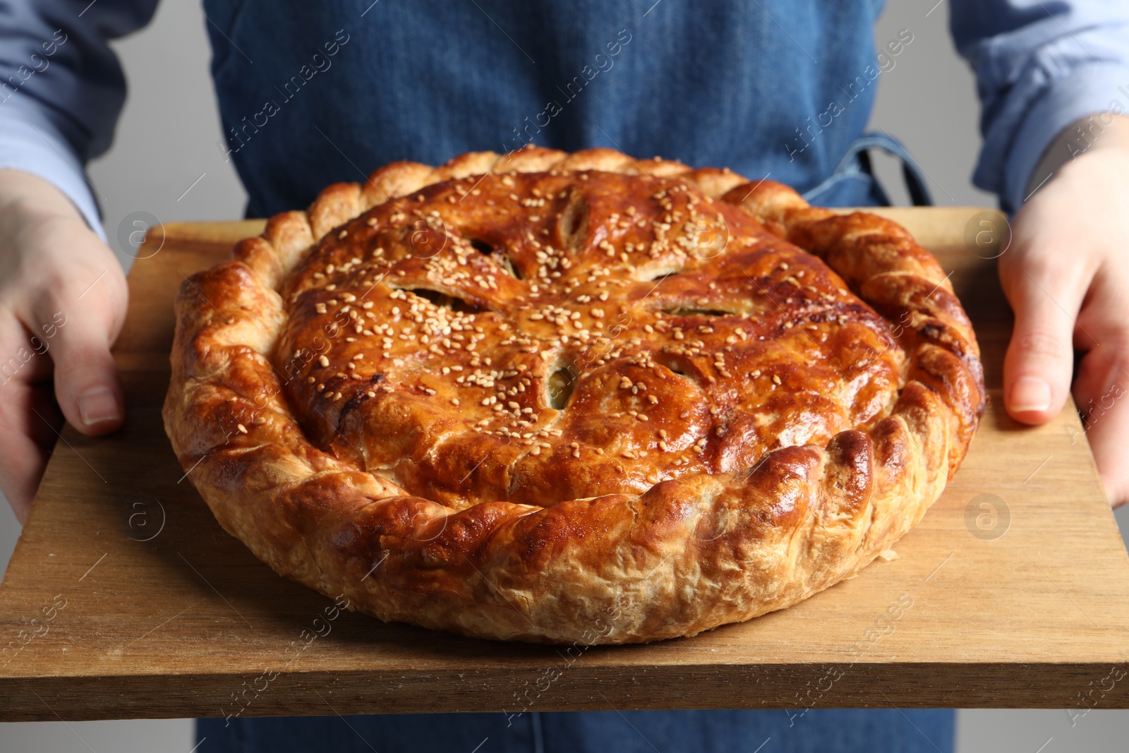 Photo of Woman holding tasty homemade pie on light grey background, closeup