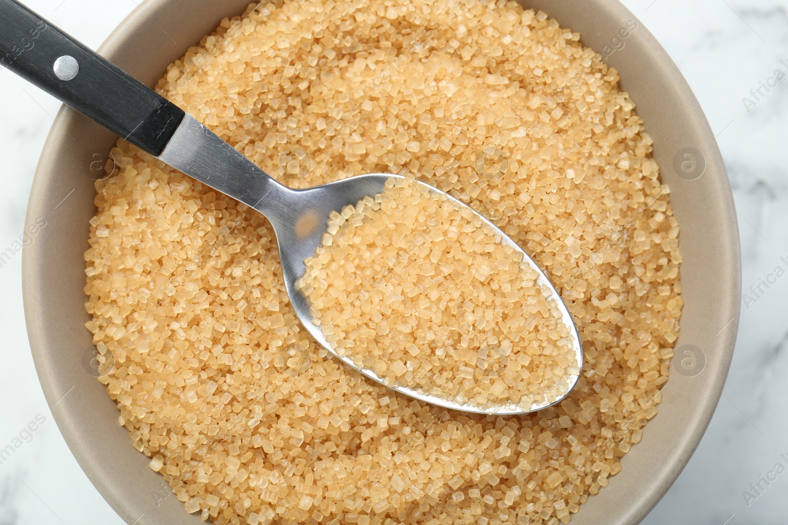 Photo of Brown sugar in bowl and spoon on white table, top view