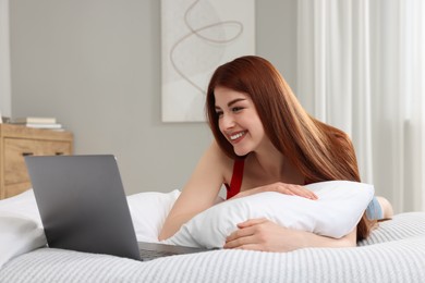 Happy woman with laptop on bed in bedroom