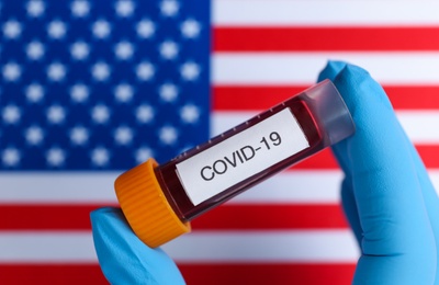 Photo of Scientist holding test tube with blood sample over American flag, closeup. Coronavirus pandemic in USA