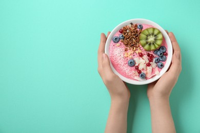 Woman holding tasty smoothie bowl with fresh kiwi fruit, berries and granola at turquoise table, top view. Space for text