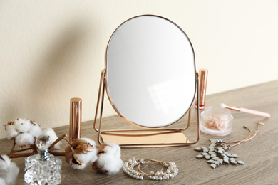 Photo of Mirror, jewelry and makeup products on wooden table near light wall