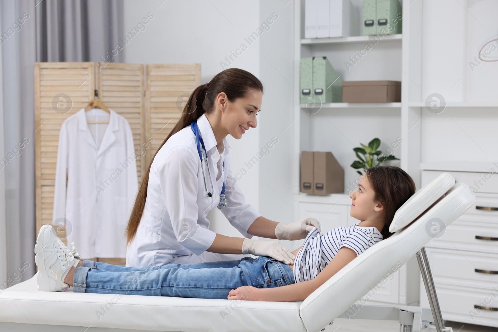 Photo of Gastroenterologist examining girl with stomach ache on couch in clinic