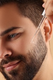 Photo of Handsome man applying cosmetic serum onto face, closeup