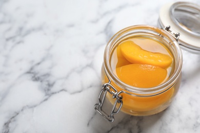 Glass jar with conserved peach halves on marble background. Space for text