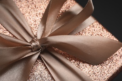 Photo of Shiny gift box with golden bow on black background, closeup