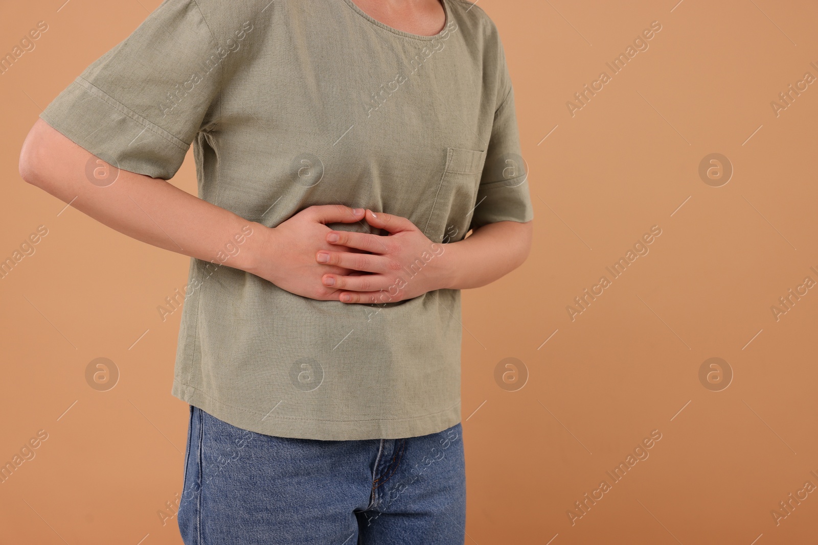 Photo of Woman suffering from abdominal pain on beige background, closeup and space for text. Unhealthy stomach