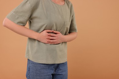 Woman suffering from abdominal pain on beige background, closeup and space for text. Unhealthy stomach