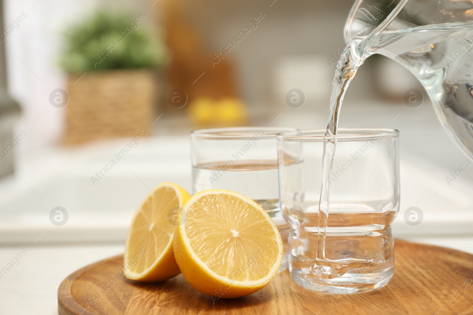 Photo of Pouring water from jug into glass on table in kitchen, closeup. Space for text