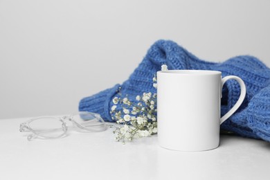 Photo of Ceramic mug, blue knitted sweater, glasses and beautiful dry flowers on white table