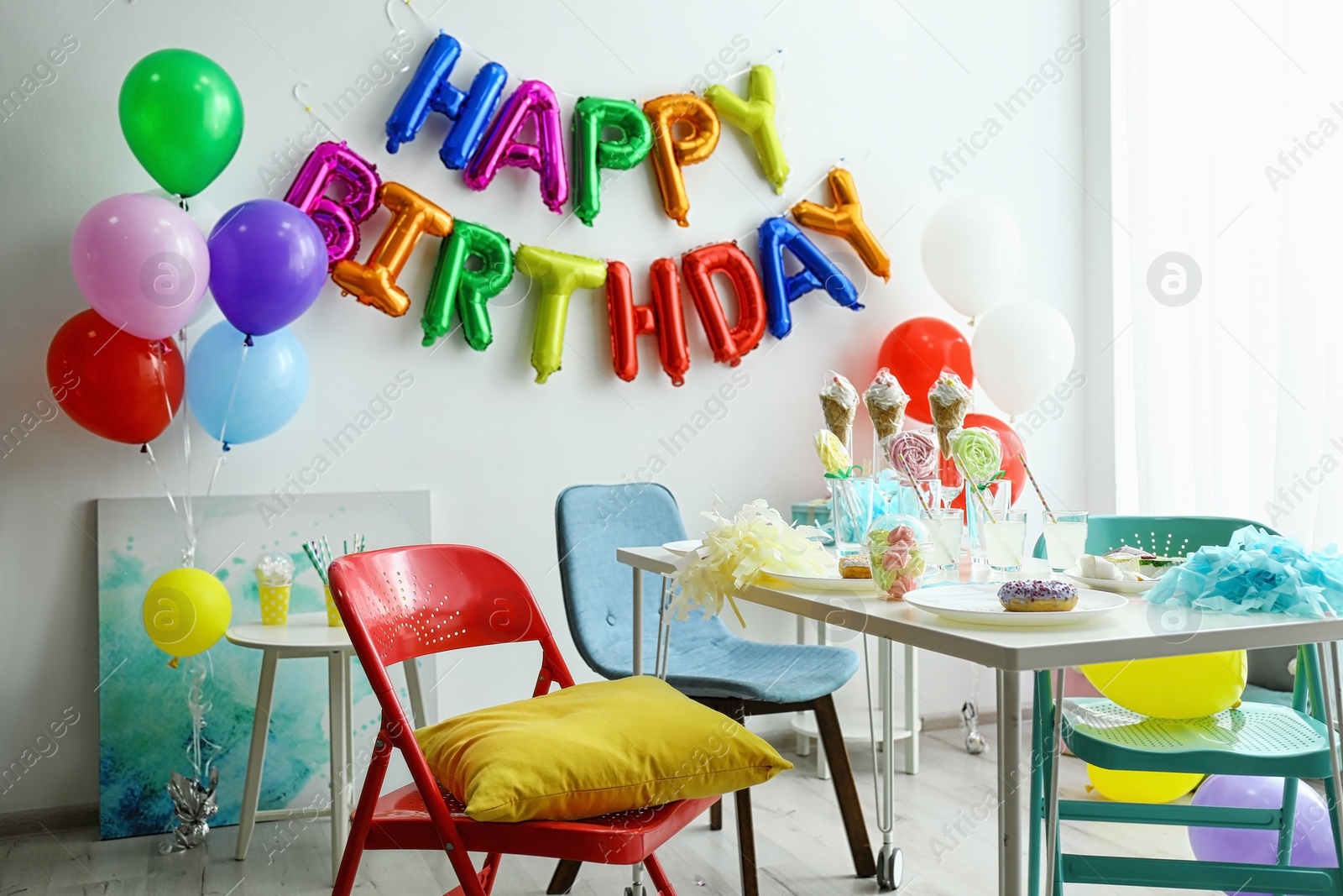 Photo of Table with treats and phrase HAPPY BIRTHDAY made of colorful balloon letters in living room