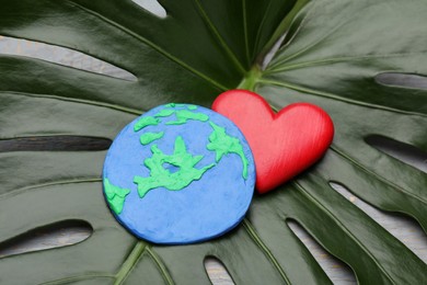 Photo of Happy Earth Day. Planet made of plasticine and decorative heart on green leaf, closeup
