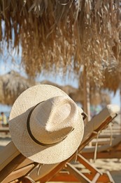 Photo of Stylish straw hat on wooden sunbed at beach