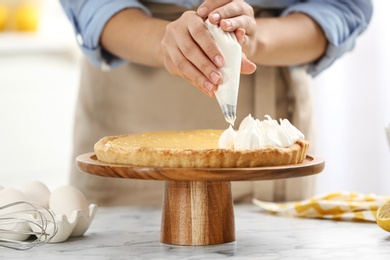 Woman preparing lemon meringue pie at white marble table in kitchen, closeup
