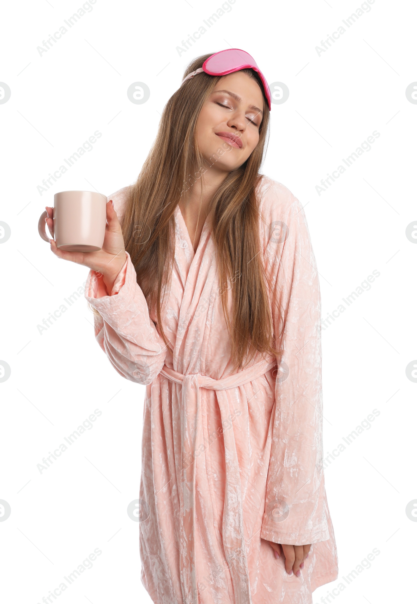 Photo of Young woman in bathrobe with sleep mask and cup of beverage on white background