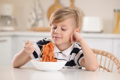 Photo of Happy boy eating tasty pasta at table in kitchen