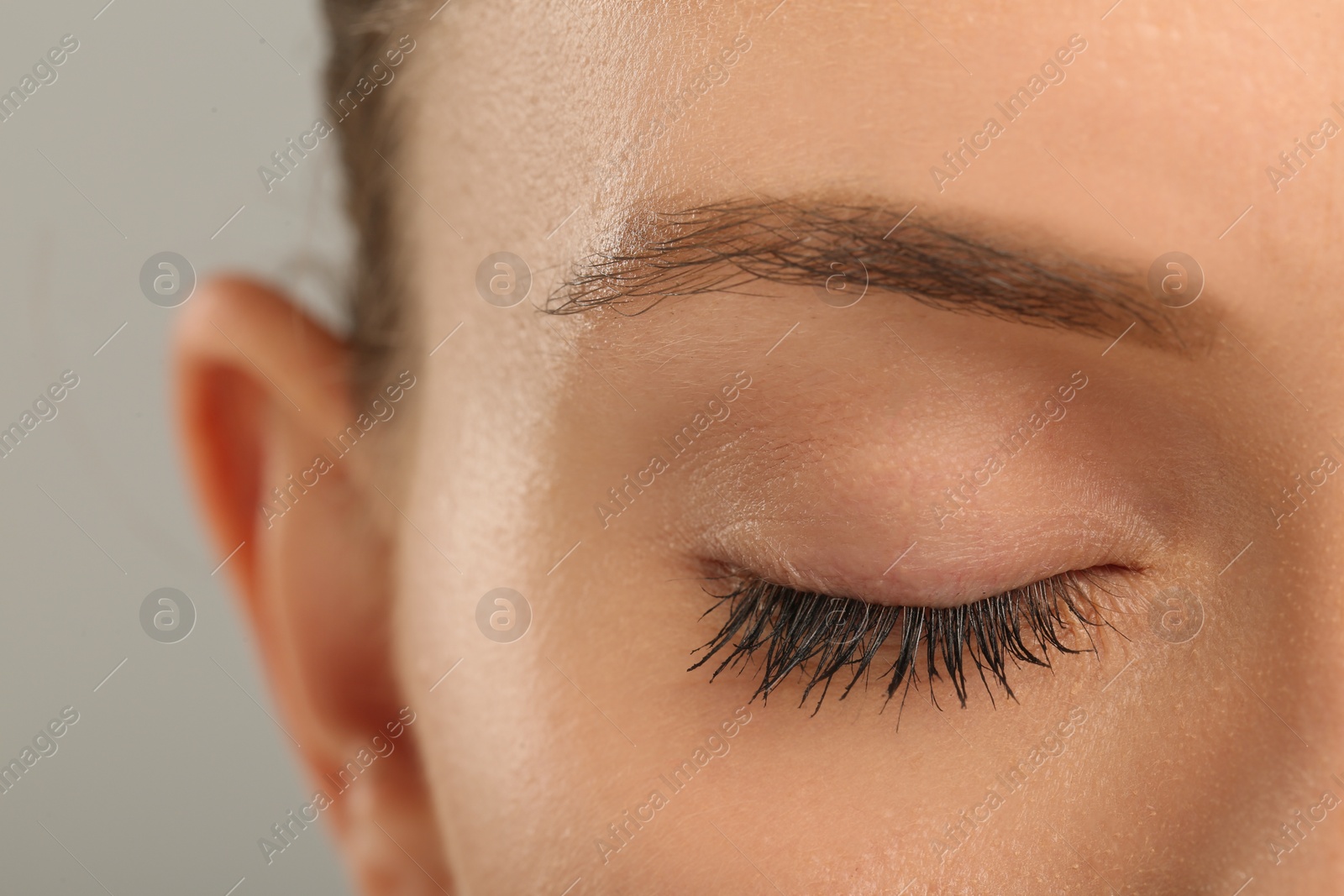 Photo of Woman with long eyelashes after mascara applying against grey background, closeup