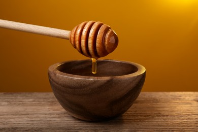 Pouring honey from dipper into bowl at wooden table against golden background