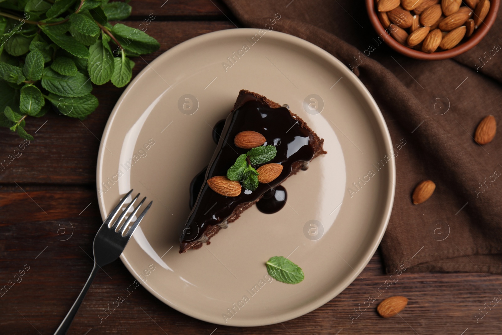 Photo of Piece of tasty homemade chocolate cake with mint and almonds on wooden table, flat lay