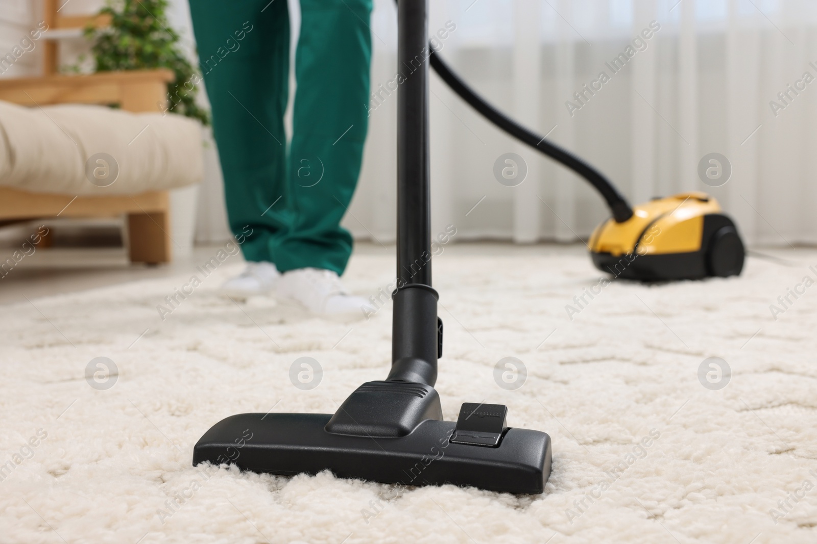 Photo of Dry cleaner's employee hoovering carpet with vacuum cleaner indoors, closeup