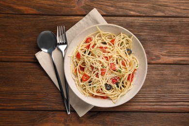 Photo of Bowl of delicious pasta with olives, tomatoes and parmesan cheese served on wooden table, flat lay