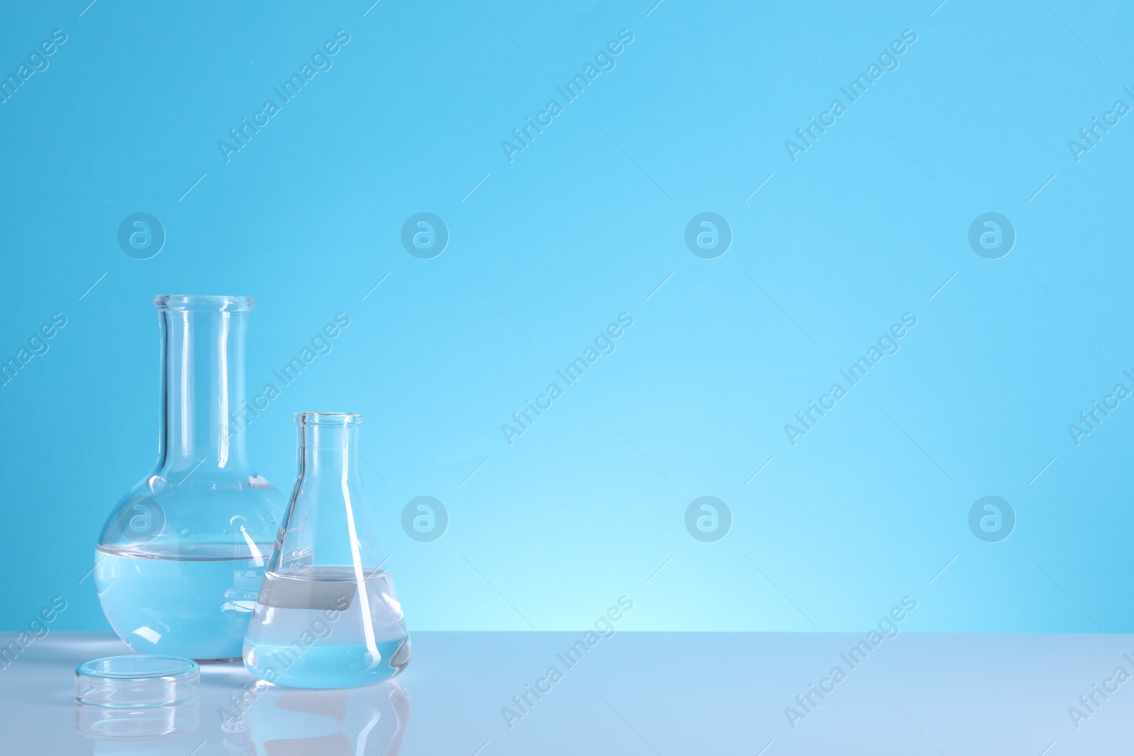 Photo of Laboratory analysis. Glass flasks on table against light blue background, space for text