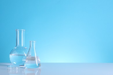 Laboratory analysis. Glass flasks on table against light blue background, space for text