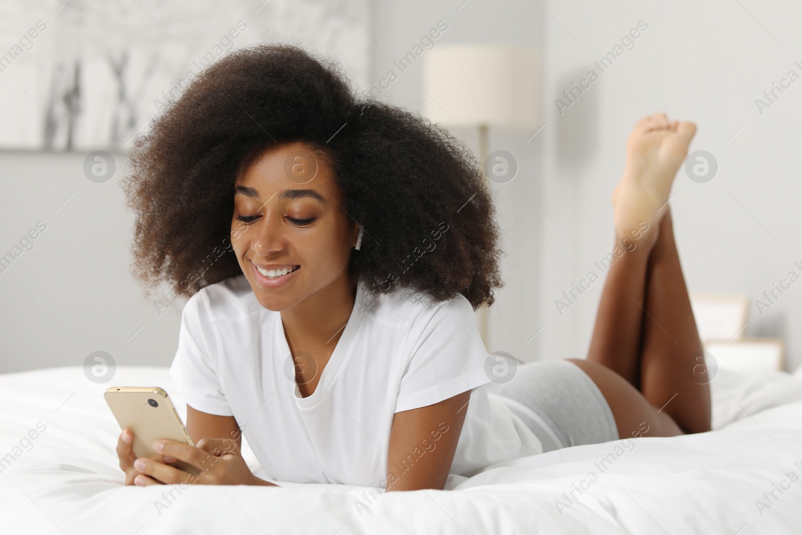 Photo of Beautiful woman in stylish underwear and t-shirt using smartphone on bed indoors