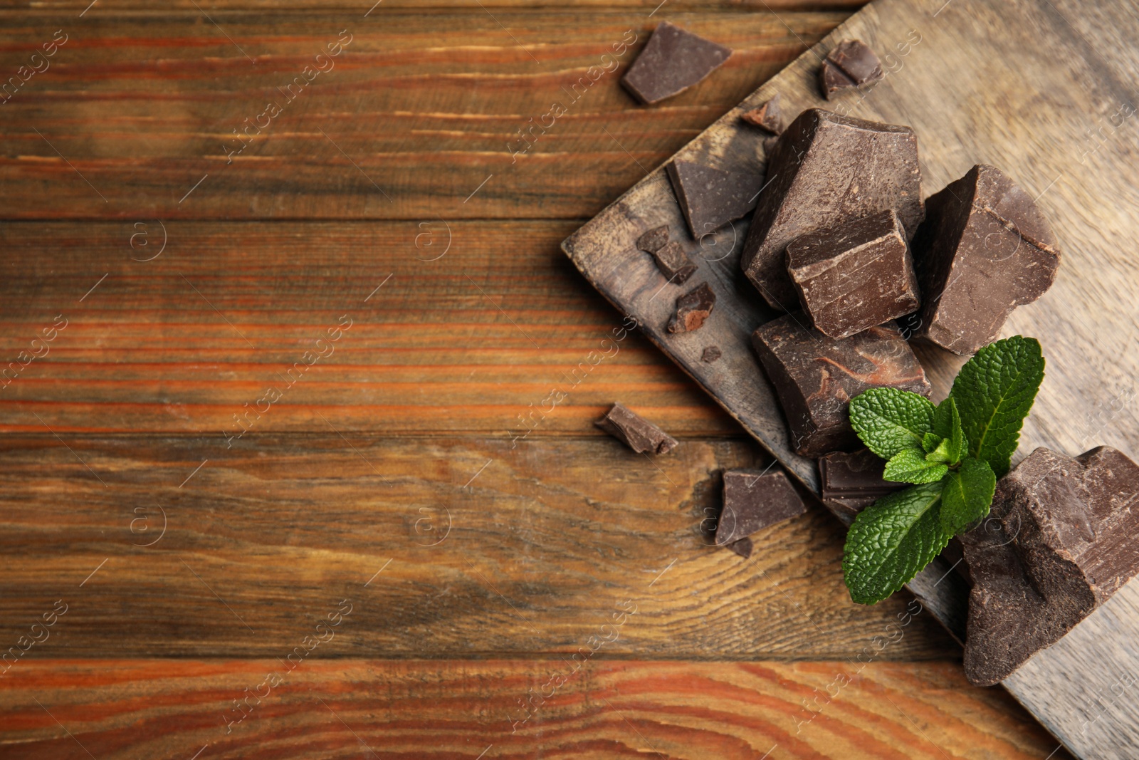 Photo of Tasty dark chocolate pieces with mint on wooden table, flat lay. Space for text