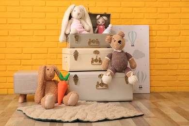 Storage trunks with different toys, pouf and picture near yellow brick wall indoors. interior design